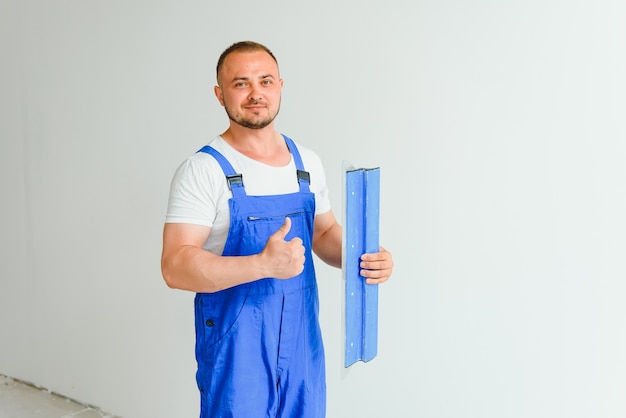 Ritratto di un lavoratore in tuta e con in mano una spatola sullo sfondo del muro intonacato. Lavori di riparazione e concetto di costruzione