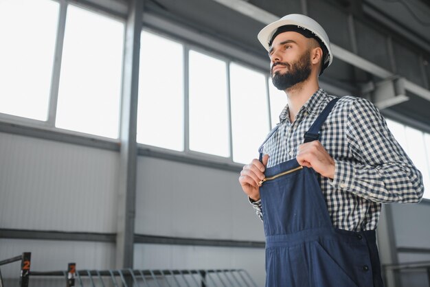 Ritratto di un lavoratore ingegnere professionista dell'industria pesante che indossa un cappello rigido uniforme di sicurezza sorridente sullo sfondo Grande fabbrica industriale sfocata