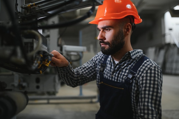 Ritratto di un lavoratore ingegnere professionista dell'industria pesante che indossa un cappello rigido uniforme di sicurezza sorridente sullo sfondo Grande fabbrica industriale sfocata