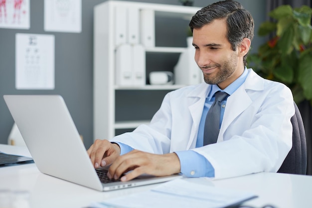Ritratto di un medico serio che utilizza il computer portatile in studio medico