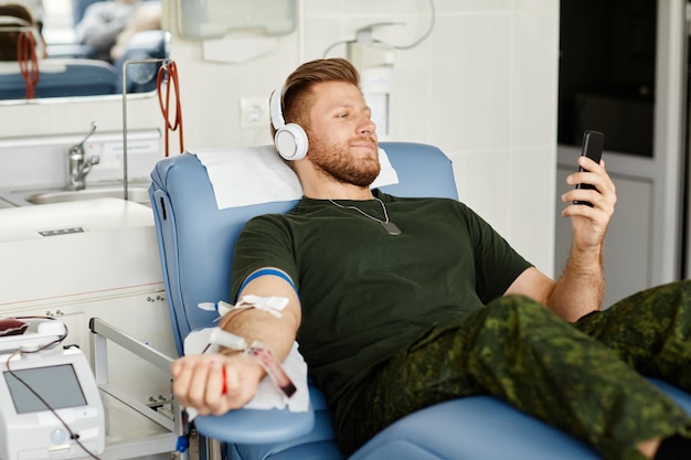 Ritratto di un militare sorridente che dà sangue mentre è sdraiato su una sedia al centro di donazione di sangue e hol