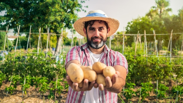 Ritratto di un moderno contadino barbuto con patate sulle mani che guarda l'obbiettivo