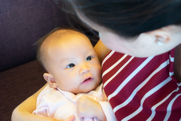 Ritratto di un neonato carino nelle mani della madre. Bella mamma che tiene risata sveglia del figlio. Primo piano di metà donna con il suo bambino. Nuova famiglia e concetto d'amore.