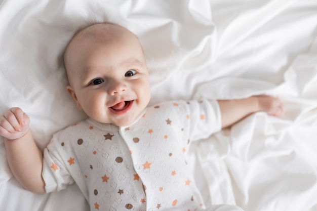 Ritratto di un neonato sorridente carino sdraiato sulla schiena su un lenzuolo bianco lifestyle home