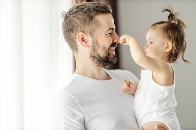 Ritratto di un padre felice che tiene in braccio la sua graziosa bambina mentre gioca con il suo naso