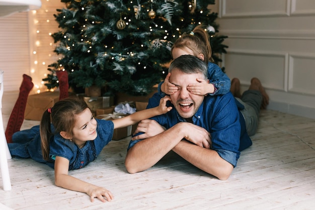 Ritratto di un padre felice e delle sue piccole figlie che giocano a casa la vigilia di Natale. famiglia felice