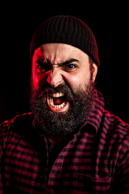 Ritratto di un pericoloso uomo arrabbiato che urla su sfondo nero con una luce rossa da dietro
