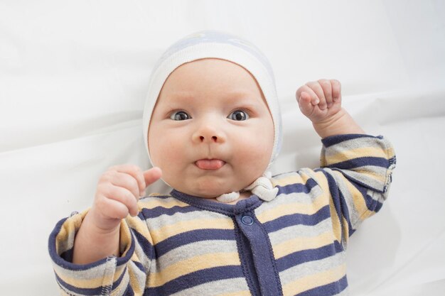 Ritratto di un piccolo bambino con una faccia divertente di espressione sul foglio bianco. Disposizione piana, vista dall'alto.