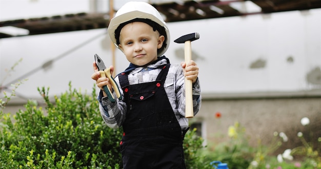 Ritratto di un piccolo costruttore in un casco bianco con un martello e una pinza in mano