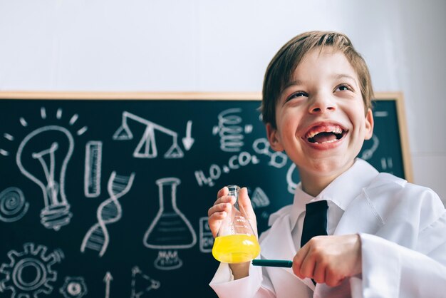Ritratto di un piccolo scienziato felice che ride mentre mostra liquido giallo in un pallone con un pennarello