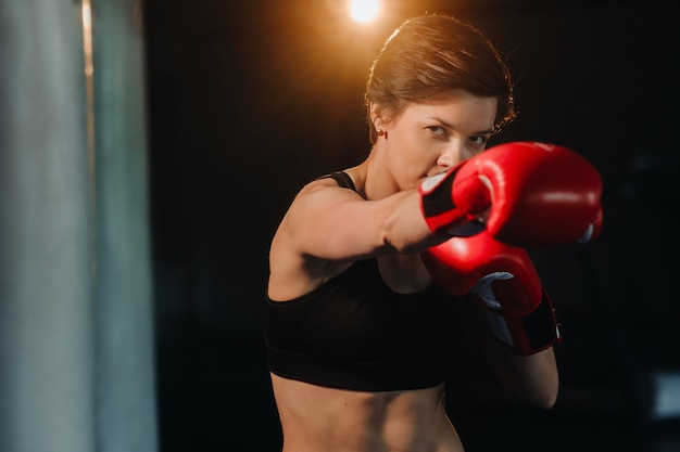 Ritratto di un pugile femminile in guanti rossi in palestra durante l'allenamento