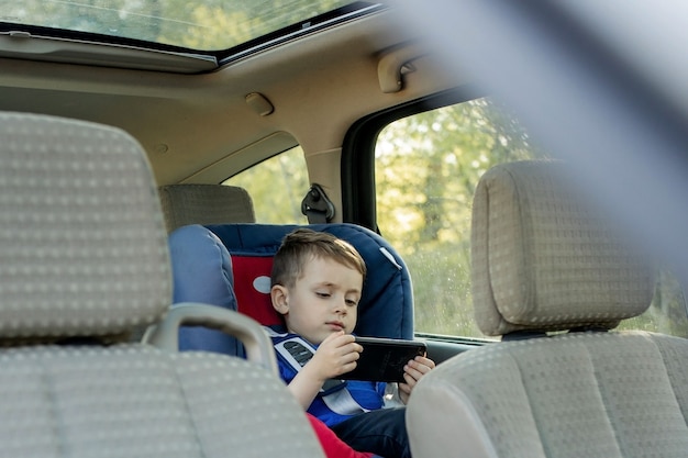 Ritratto di un ragazzino annoiato seduto in un seggiolino per auto. Sicurezza del trasporto dei bambini.