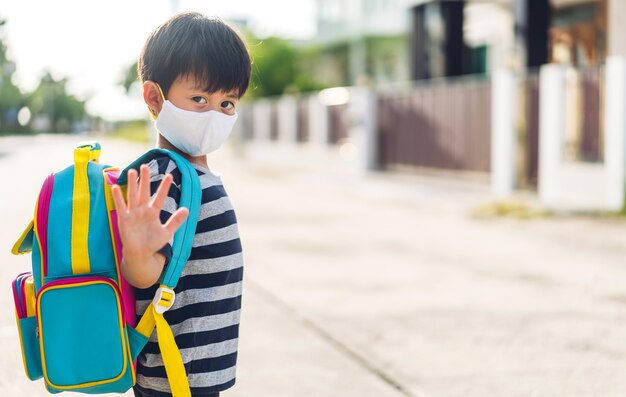 Ritratto di un ragazzino asiatico asiatico che indossa una maschera di sicurezza protettiva in quarantena per il coronavirus con allontanamento sociale pronto a tornare a scuola dopo il covid-19 con lo zaino. Ritorno al concetto di scuola