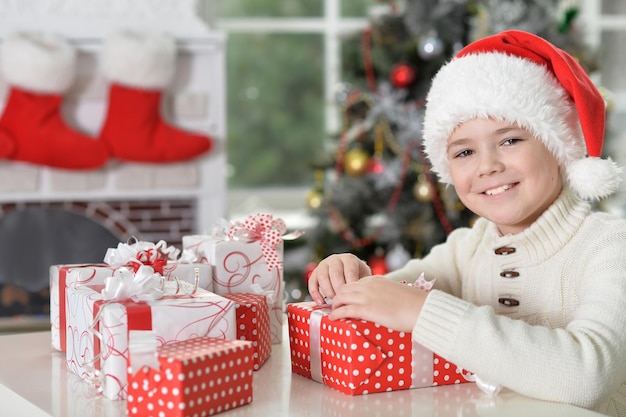 Ritratto di un ragazzino carino con un cappello da Babbo Natale con regali per Natale a casa