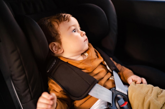 Ritratto di un ragazzino carino seduto in un seggiolino auto nero allacciato con cinture di sicurezza