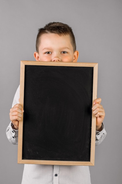 Ritratto di un ragazzino che tiene una tavola su sfondo grigio