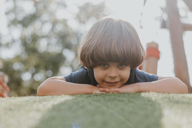 Ritratto di un ragazzino con una maglietta blu sdraiato sull'erba verde. bambino sta giocando nel parco. attività all'aperto, stile di vita. spazio per il testo. Foto di alta qualità