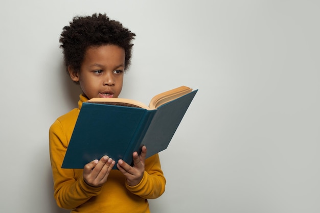 Ritratto di un ragazzino nero che legge un libro su sfondo bianco