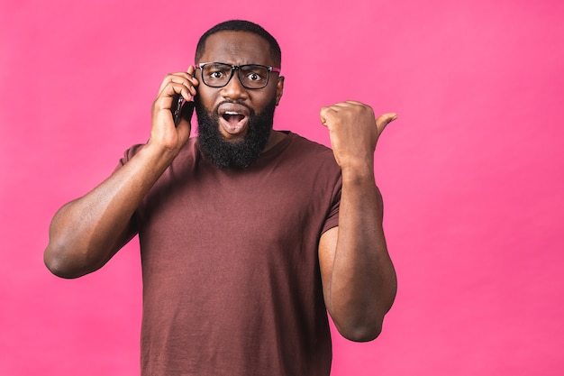 Ritratto di un ragazzo afroamericano felice che parla al telefono cellulare isolato su sfondo rosa. Dito puntato.