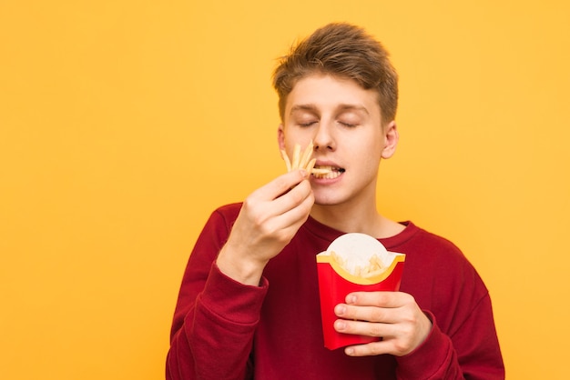 Ritratto di un ragazzo che mangia patatine fritte con gli occhi chiusi su un giallo