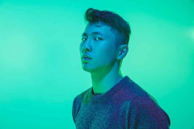 Ritratto di un ragazzo con luce al neon colorata su sfondo verde studio. Modello maschile dall'umore calmo e serio. Espressione facciale, cyberpunk, stile di vita e aspetto dei millennial. Futuro, tecnologie.