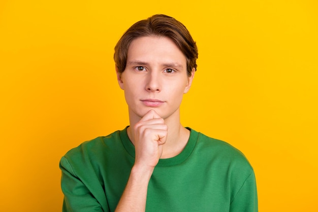 Ritratto di un ragazzo dai capelli castani concentrato serio che pensa toccando il mento isolato su uno sfondo di colore brillante