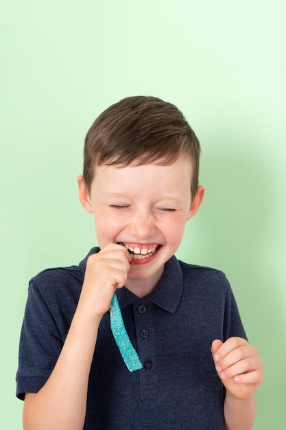 Ritratto di un ragazzo di 7 anni con una polo blu morde un lungo nastro di marmellata acida e strizza gli occhi al gusto di una smorfia