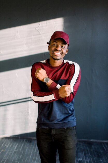 Ritratto di un ragazzo hipster afroamericano vestito con un maglione in pile rosso e berretto rosso in studio. Isolato su sfondo scuro con texture studente indossando abiti sportivi