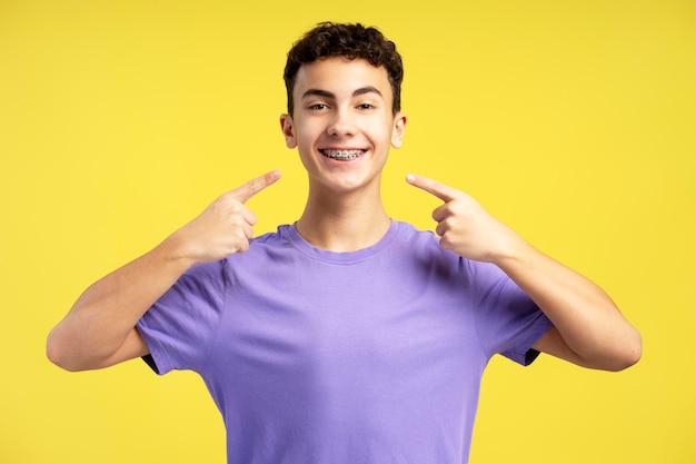 Ritratto di un ragazzo positivo che indossa una maglietta casual che guarda la fotocamera che punta il dito contro l'apparecchio dentale