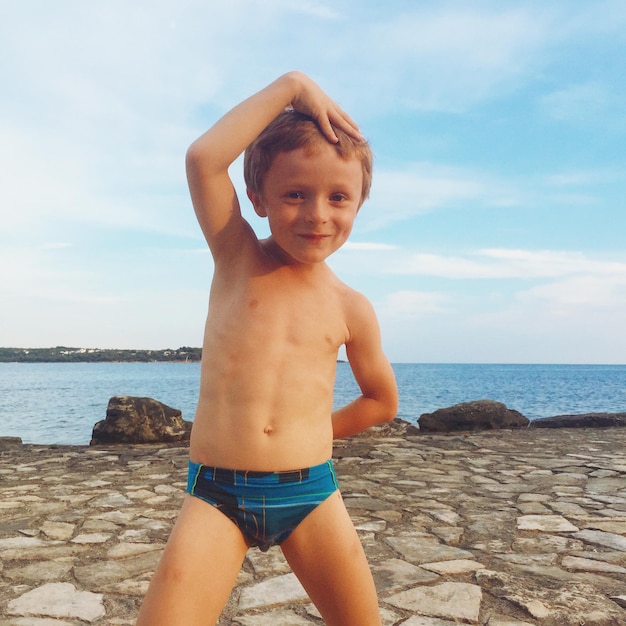 Ritratto di un ragazzo senza camicia sorridente in piedi sulla passerella con il mare sullo sfondo