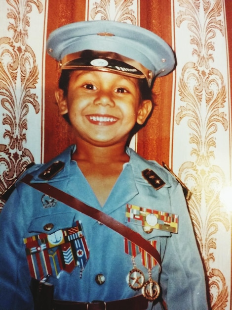 Ritratto di un ragazzo sorridente che indossa l'uniforme militare contro la tenda