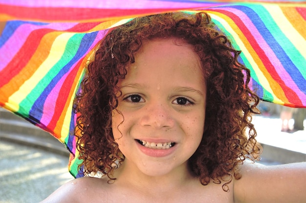 Ritratto di un ragazzo sorridente con i capelli ricci bagnati e tessuti colorati