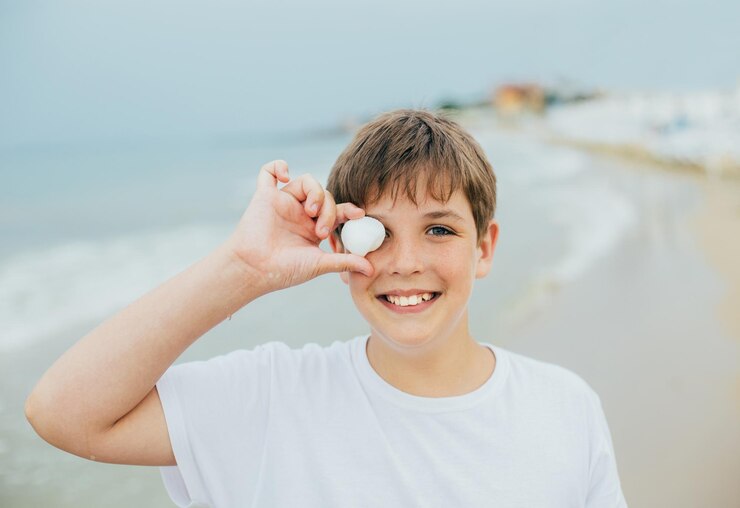 Ritratto di un ragazzo sulla spiaggia con un guscio che copre il suo occhio sullo sfondo del mare