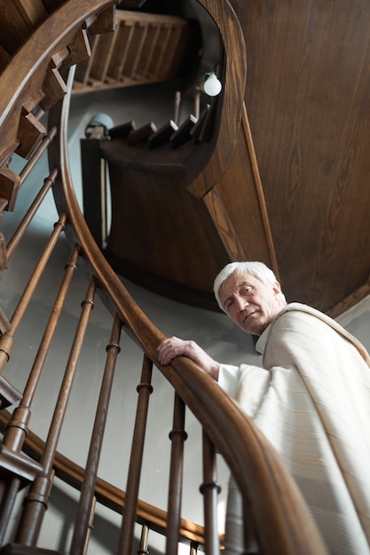 Ritratto di un sacerdote anziano che guarda la telecamera mentre sale le scale di legno