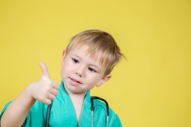 Ritratto di un simpatico ragazzino caucasico vestito di verde medico che mostra il gesto del pollice su sfondo giallo