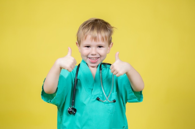Ritratto di un simpatico ragazzino caucasico vestito di verde medico che mostra il gesto del pollice su sfondo giallo