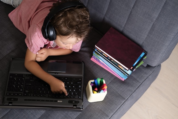 Ritratto di un simpatico ragazzo caucasico che utilizza laptop e cuffie mentre studia a casa, concetto di educazione remota. Vista dall'alto. Quarantena. Torna al concetto di scuola.