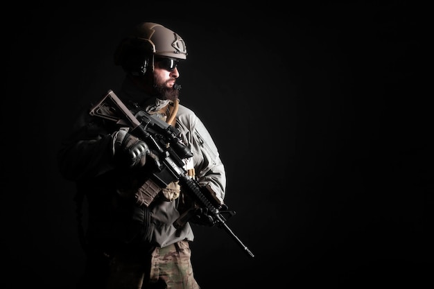 Ritratto di un soldato delle forze speciali in uniforme con un'arma su uno sfondo scuro