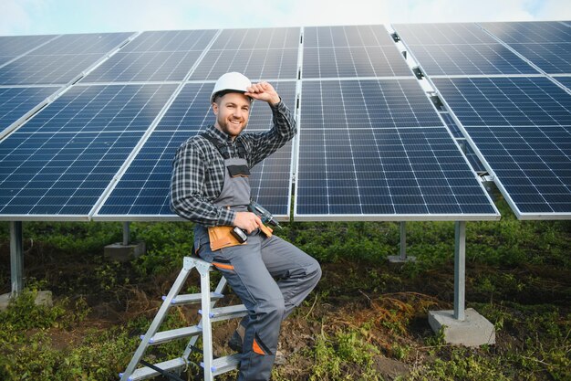 Ritratto di un tecnico tecnico sorridente e fiducioso con un cacciavite elettrico in piedi di fronte al sistema fotovoltaico esterno incompiuto del pannello solare