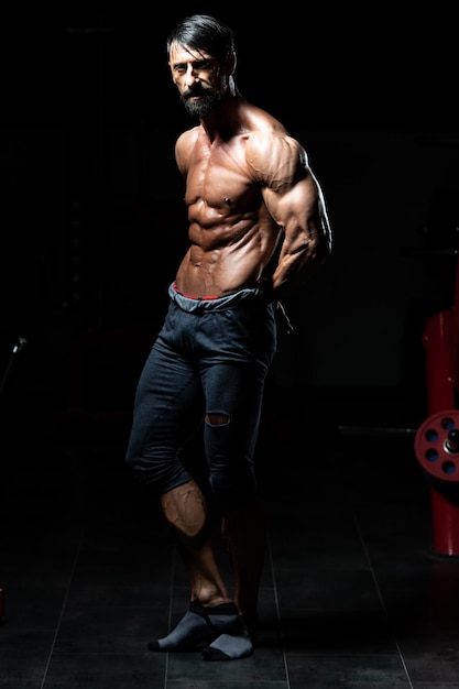 Ritratto di un uomo adulto fisicamente in forma che mostra il suo corpo ben allenato - modello di fitness bodybuilder atletico muscolare in posa dopo gli esercizi