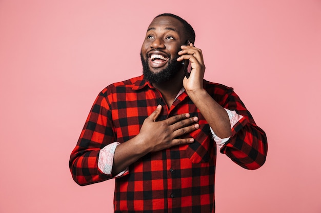 Ritratto di un uomo africano casual felice in piedi isolato, parlando al telefono cellulare