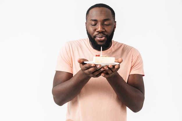 Ritratto di un uomo africano felice ed eccitato che indossa una camicia in piedi isolato, con in mano un piatto con una torta di compleanno