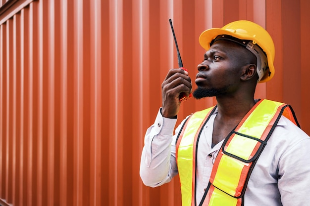 Ritratto di un uomo africano ingegnere o operaio industriale con casco e giubbotto che parla alla radio