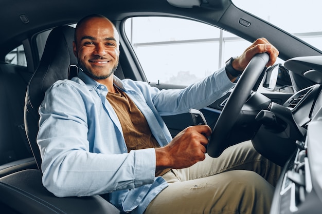 Ritratto di un uomo afroamericano felice bello che si siede nella nuova automobile