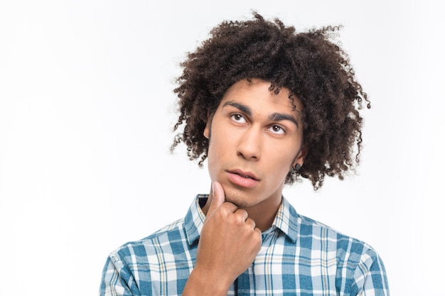 Ritratto di un uomo afroamericano pensieroso con i capelli ricci che cerca isolato su un muro bianco