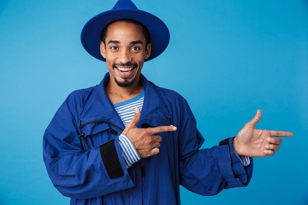 Ritratto di un uomo afroamericano sorridente che indossa un cappello che punta le dita da parte isolato su blue