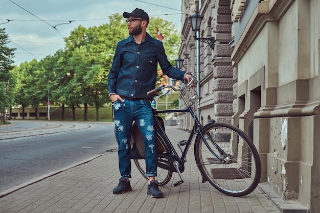 Ritratto di un uomo alla moda in abiti eleganti che cammina con la bicicletta della città sulla strada.