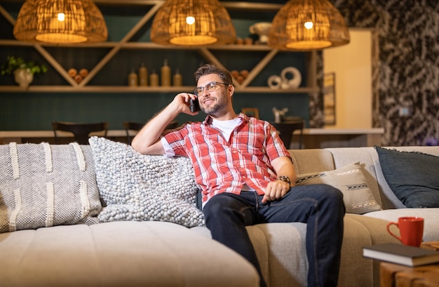 Ritratto di un uomo allegro con smart phone di notte ragazzo di casa che usa il telefono a casa stuoia mediorientale