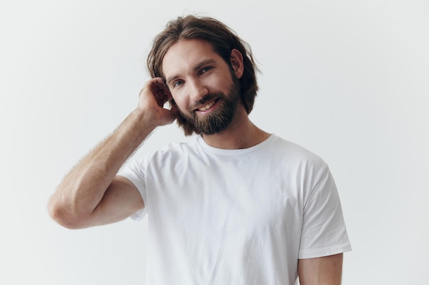 Ritratto di un uomo allegro con una folta barba nera e capelli lunghi con un sorriso gentile in una maglietta bianca su sfondo bianco isolato