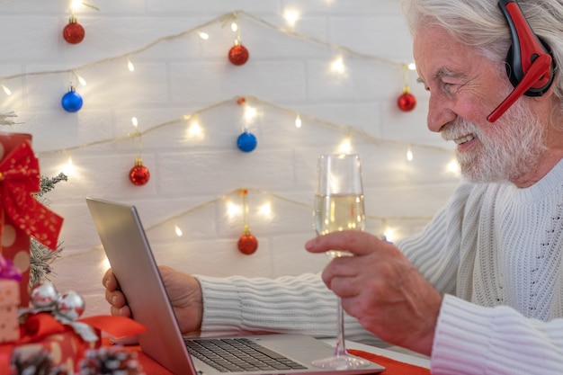 Ritratto di un uomo anziano a Natale che indossa le cuffie utilizzando la videochiamata del laptop con persone distanti